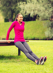 Image showing smiling woman doing push-ups on bench outdoors