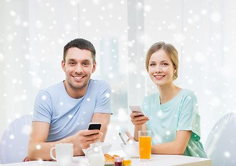 Image showing smiling couple with smartphones having breakfast