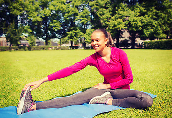 Image showing smiling woman stretching leg on mat outdoors