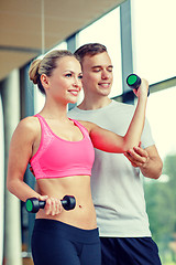 Image showing smiling young woman with personal trainer in gym