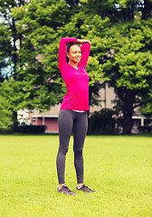 Image showing smiling black woman stretching leg outdoors