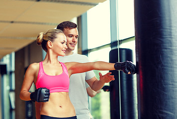 Image showing smiling woman with personal trainer boxing in gym