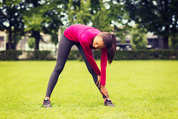 Image showing smiling black woman stretching leg outdoors