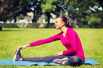 Image showing smiling woman stretching leg on mat outdoors