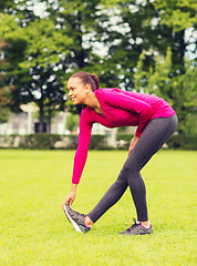 Image showing smiling black woman stretching leg outdoors