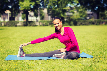 Image showing smiling woman stretching leg on mat outdoors