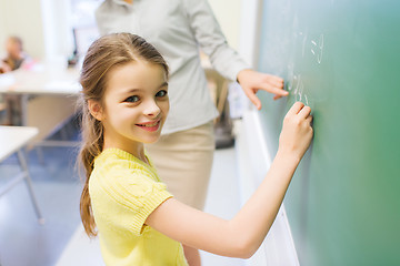 Image showing little smiling schoolgirl writing on chalk board