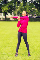 Image showing smiling black woman stretching leg outdoors