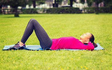 Image showing smiling woman doing exercises on mat outdoors