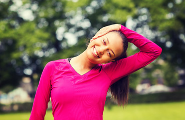Image showing smiling black woman stretching leg outdoors