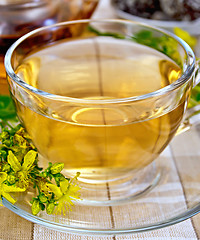 Image showing Tea from tutsan in glass cup on tablecloth with teapot