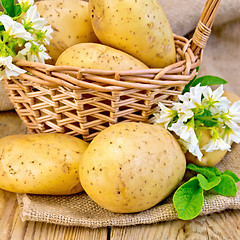 Image showing Potatoes yellow with flower and basket on board and sackcloth