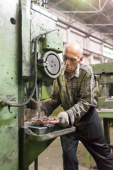 Image showing Elderly worker drills bores on detail by driller