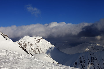 Image showing Sunlit off-piste slope and mountains in dark clouds