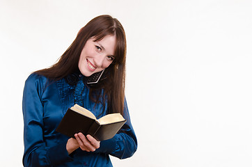 Image showing Business woman writing in a notebook on the phone