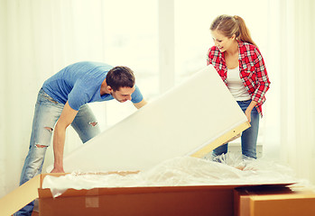 Image showing smiling couple opening big cardboard box with sofa