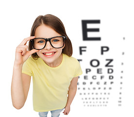 Image showing smiling little girl in eyeglasses with eye chart