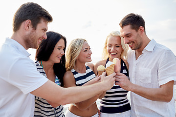 Image showing smiling friends eating ice cream on beach