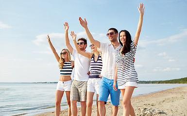 Image showing smiling friends walking on beach and waving hands