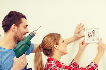 Image showing smiling couple drilling hole in wall at home