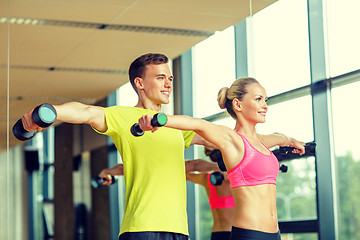 Image showing smiling man and woman with dumbbells in gym