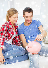 Image showing smiling couple with piggybank sitting on sofa