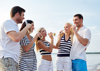 Image showing smiling friends with drinks in bottles on beach