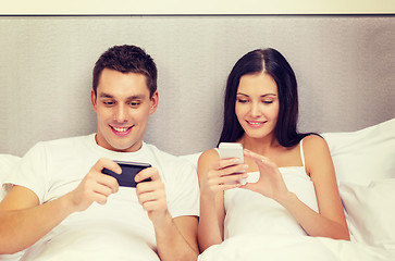 Image showing smiling couple in bed with smartphones