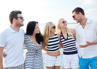 Image showing smiling friends in sunglasses talking on beach