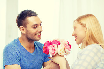 Image showing smiling man giving girfriens flowers at home
