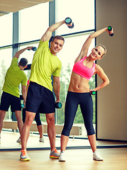 Image showing smiling man and woman with dumbbells in gym