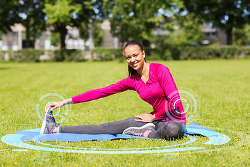 Image showing smiling woman stretching leg on mat outdoors