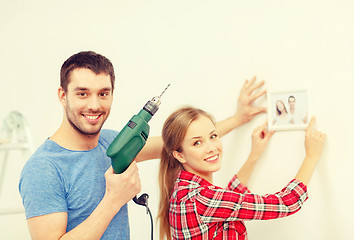 Image showing smiling couple drilling hole in wall at home