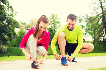 Image showing smiling couple tying shoelaces outdoors