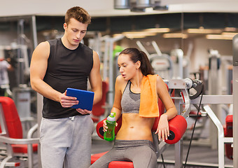 Image showing smiling young woman with personal trainer in gym