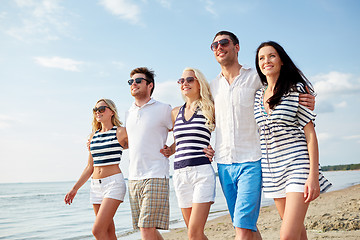 Image showing smiling friends in sunglasses walking on beach