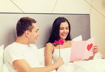 Image showing smiling couple in bed with postcard and flower