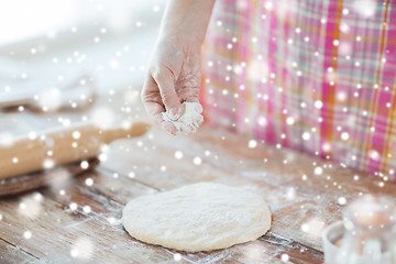 Image showing close up of woman hand sprinkling dough with flour