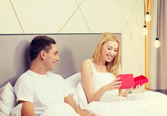 Image showing smiling couple in bed with red gift box