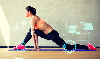 Image showing smiling woman stretching leg on mat in gym