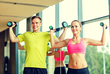 Image showing smiling man and woman with dumbbells in gym