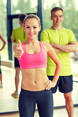 Image showing smiling man and woman showing thumbs up in gym