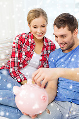 Image showing smiling couple with piggybank sitting on sofa