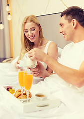 Image showing smiling couple having breakfast in bed in hotel