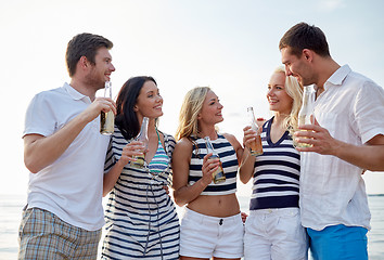 Image showing smiling friends with drinks in bottles on beach