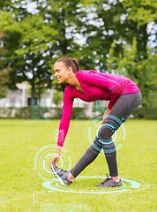 Image showing smiling woman stretching leg outdoors