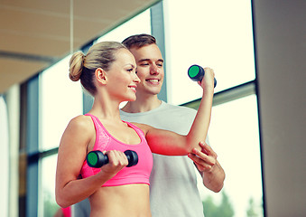 Image showing smiling young woman with personal trainer in gym