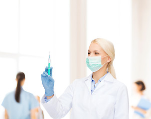 Image showing doctor in mask holding syringe with injection