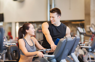 Image showing happy woman with trainer on exercise bike in gym