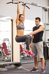 Image showing young woman with trainer doing leg raises in gym